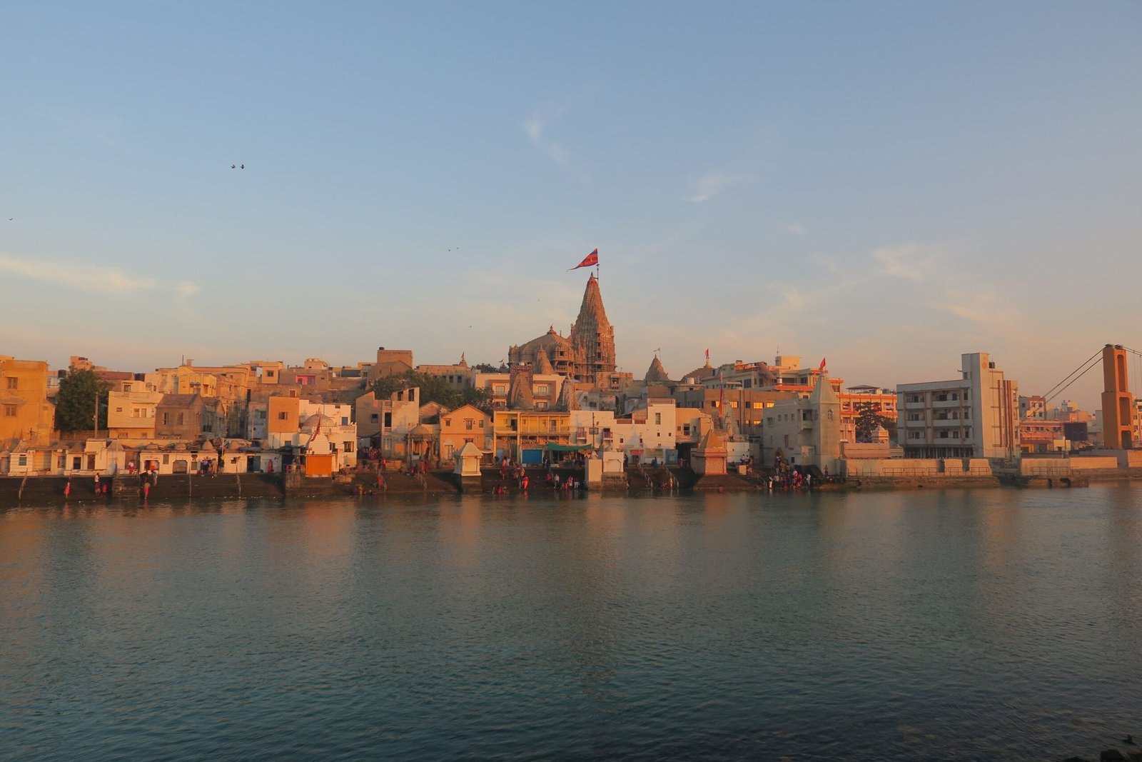 View of the historic Dwarka city and temple by the river at sunset, capturing its architectural beauty.