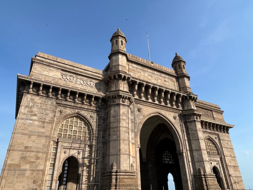 View of the iconic Gateway of India, a historical arch monument in Mumbai, captured against a bright blue sky.